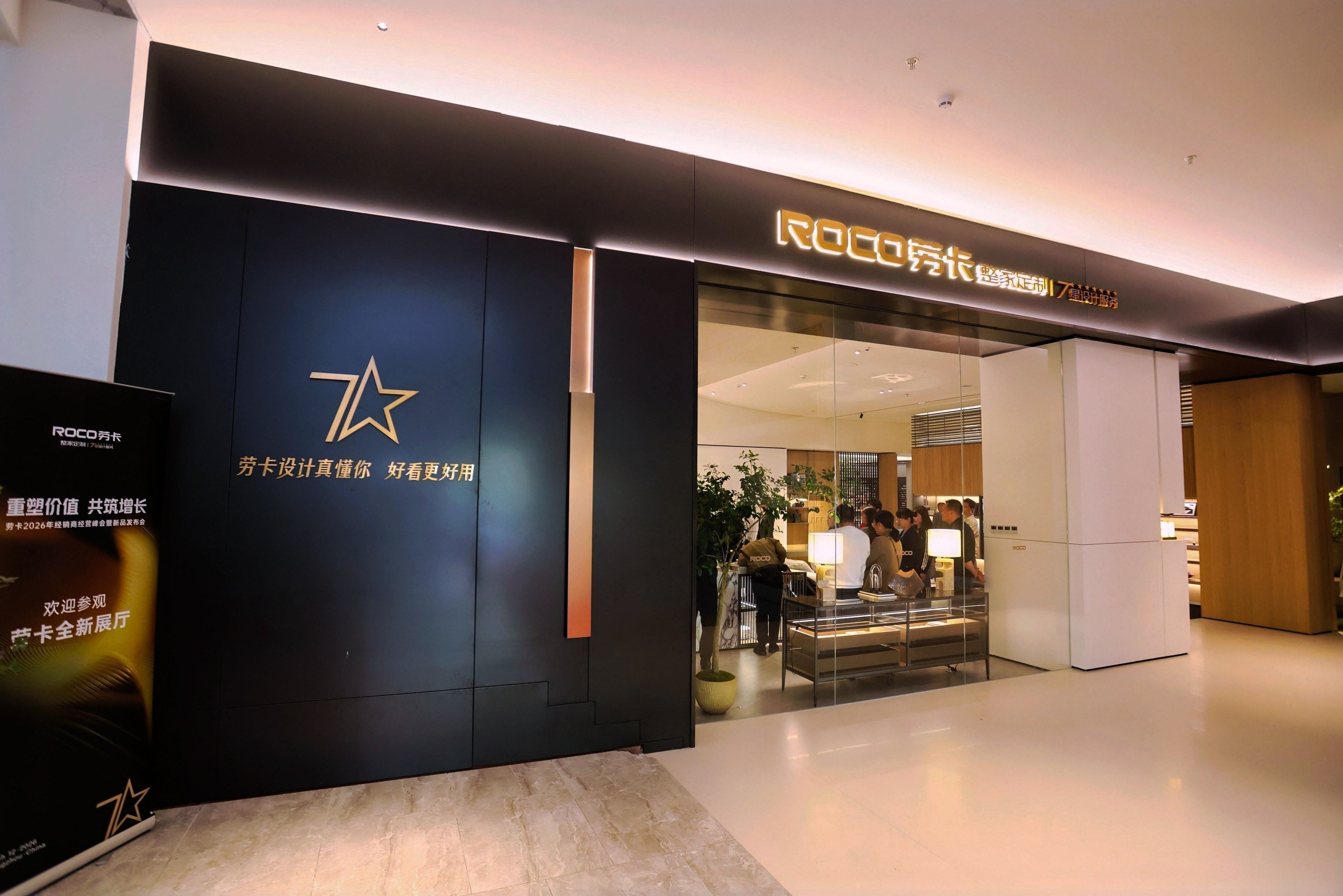 劳卡家居全新展厅入口实景，黑色极简门头搭配暖色发光字“ROCO劳卡 整家定制 7星服务”，左侧墙面印有金色七星标志及“劳卡设计真懂你 好看更好用”标语。透过玻璃